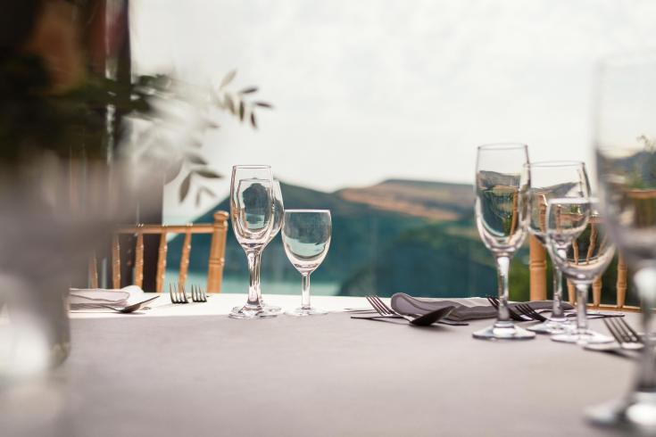 A table in The Venue at Sandy Cove set with cutlery and wine glasses and a view of the bay behind