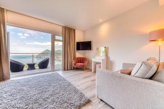 The interior of a luxury sea view room at Sandy Cove Hotel showing the seating area, balcony and view over the sea