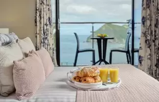 A breakfast tray with food and juice sitting on the bed in one of Sandy Cove Hotel's classic sea view with balcony rooms